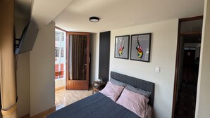 A bedroom with a bed, a TV mounted on the wall, a door, and two framed artworks. - Comfort in the heart of downtown Tacna (Tacna)