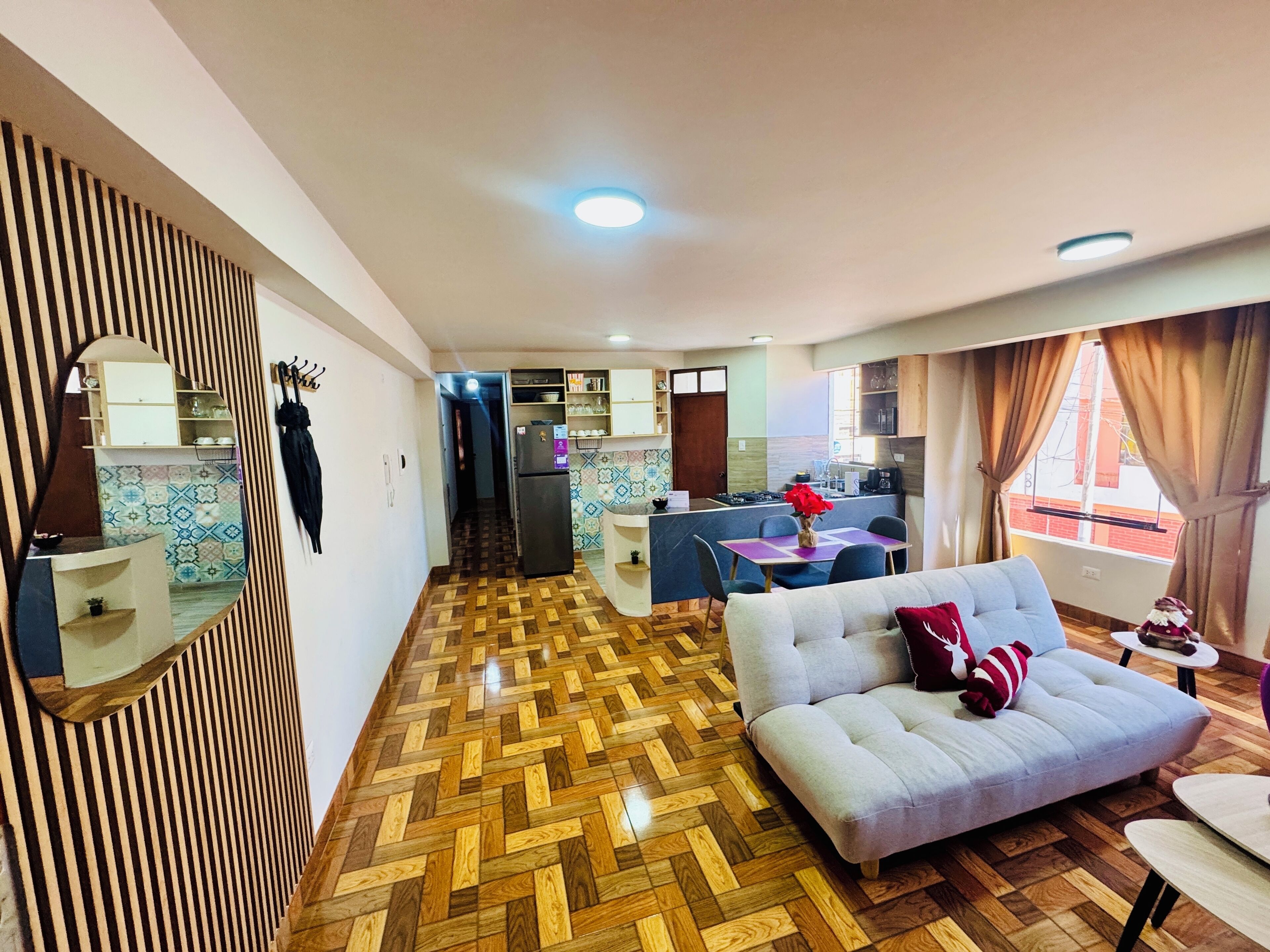 A modern living room with a herringbone wood floor, a grey sofa, and a dining area with a purple table.