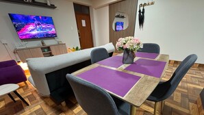 A modern dining area with a wooden herringbone floor, a large flat-screen TV, a sofa, and a table with purple placemats. - Comfort in the heart of downtown Tacna (Tacna)