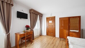 Una habitación con escritorio de madera, cama, televisor montado en la pared y armario de madera.