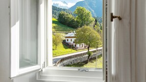Una ventana con vista a una casa, un puente de piedra y un paisaje montañoso.