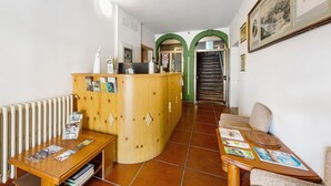 Zona de recepción con un escritorio de madera, área de espera con un sofá y sillones, y piso de baldosas.