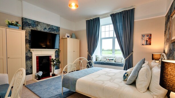 A bedroom with a bed, a fireplace, a window with curtains, a television, and a cabinet. - The Old Storehouse (Netherton Colliery)