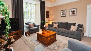 A living room with a large flat-screen TV, two grey sofas, a wooden coffee table, and a potted plant. - The Old Storehouse (Netherton Colliery)