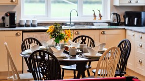 A dining area with a table set for four, a vase with flowers, and a view of a green field through a window. - The Old Storehouse (Netherton Colliery)