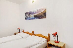 A double bed with white linens, a wooden headboard, two bedside tables with red lamps, and a wall-mounted painting of a mountain landscape. - Albergo Trieste – Room '5' with Mountain View, Shared Terrace, and Wi-Fi (Lorenzago di Cadore)