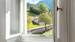 Janela com vista para uma casa, uma ponte de pedra e uma paisagem montanhosa.