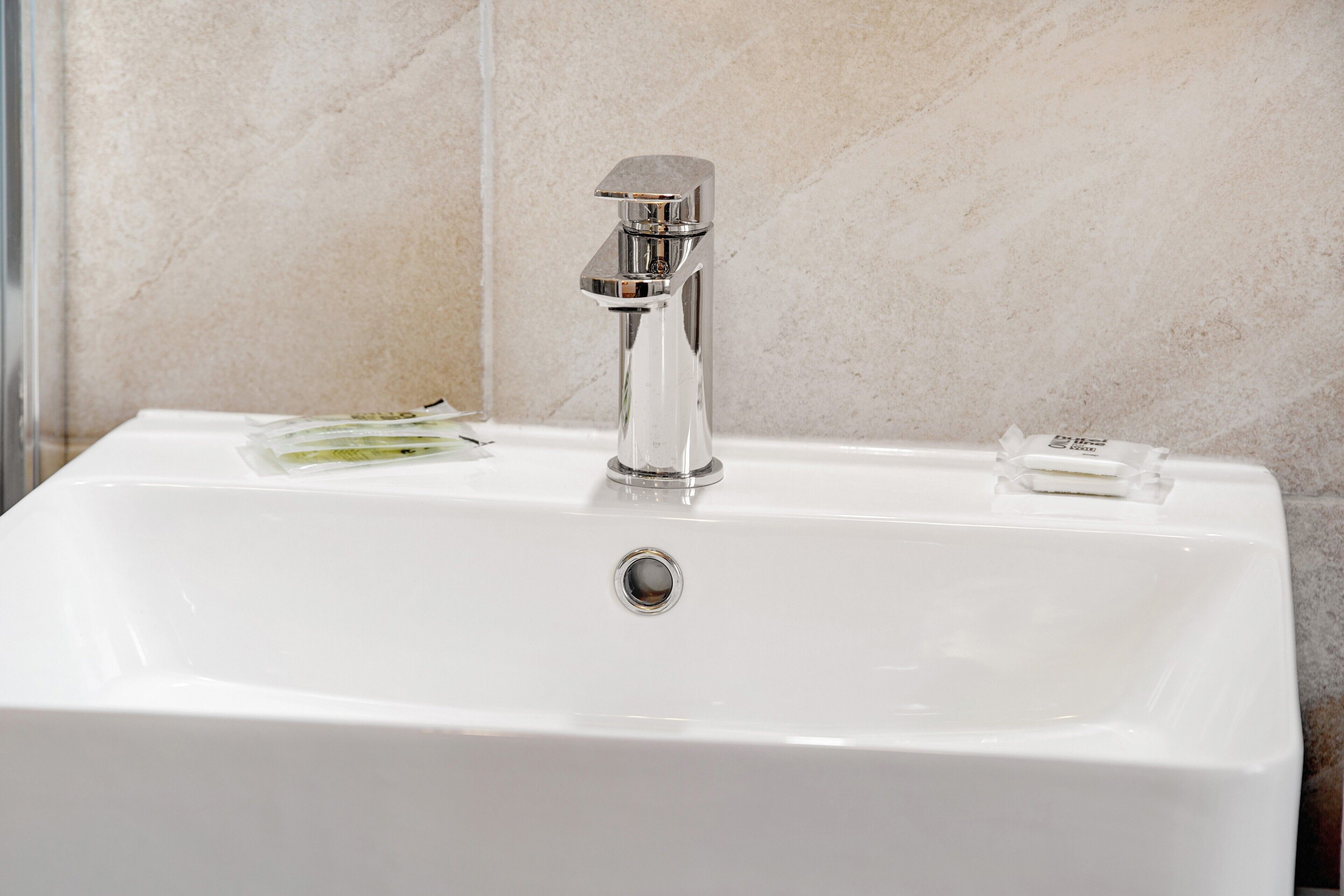 Un lavandino bianco con rubinetto cromato e dispenser per sapone.