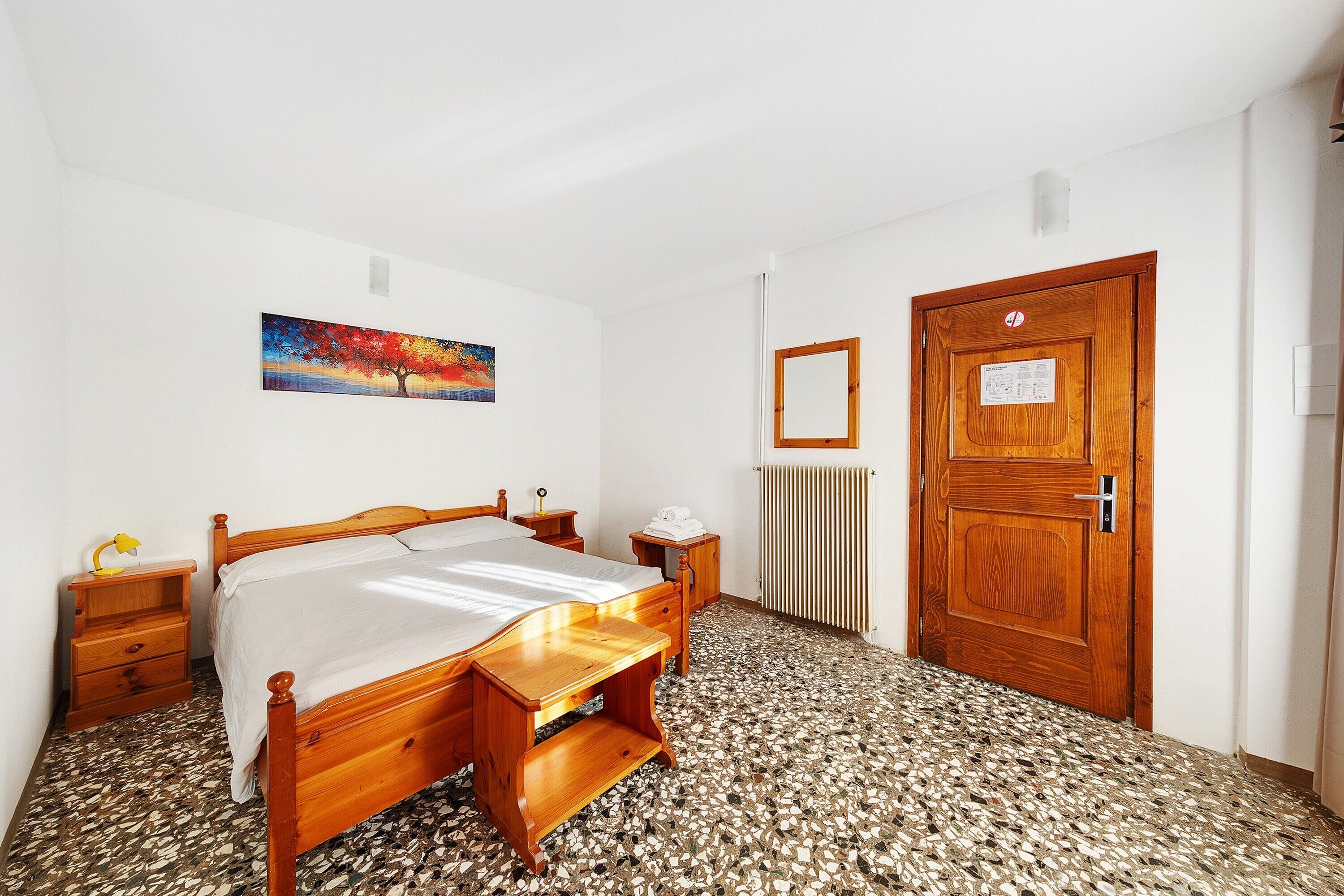 Une chambre à coucher avec un lit en bois, une table de chevet, une commode, un radiateur et une porte en bois.