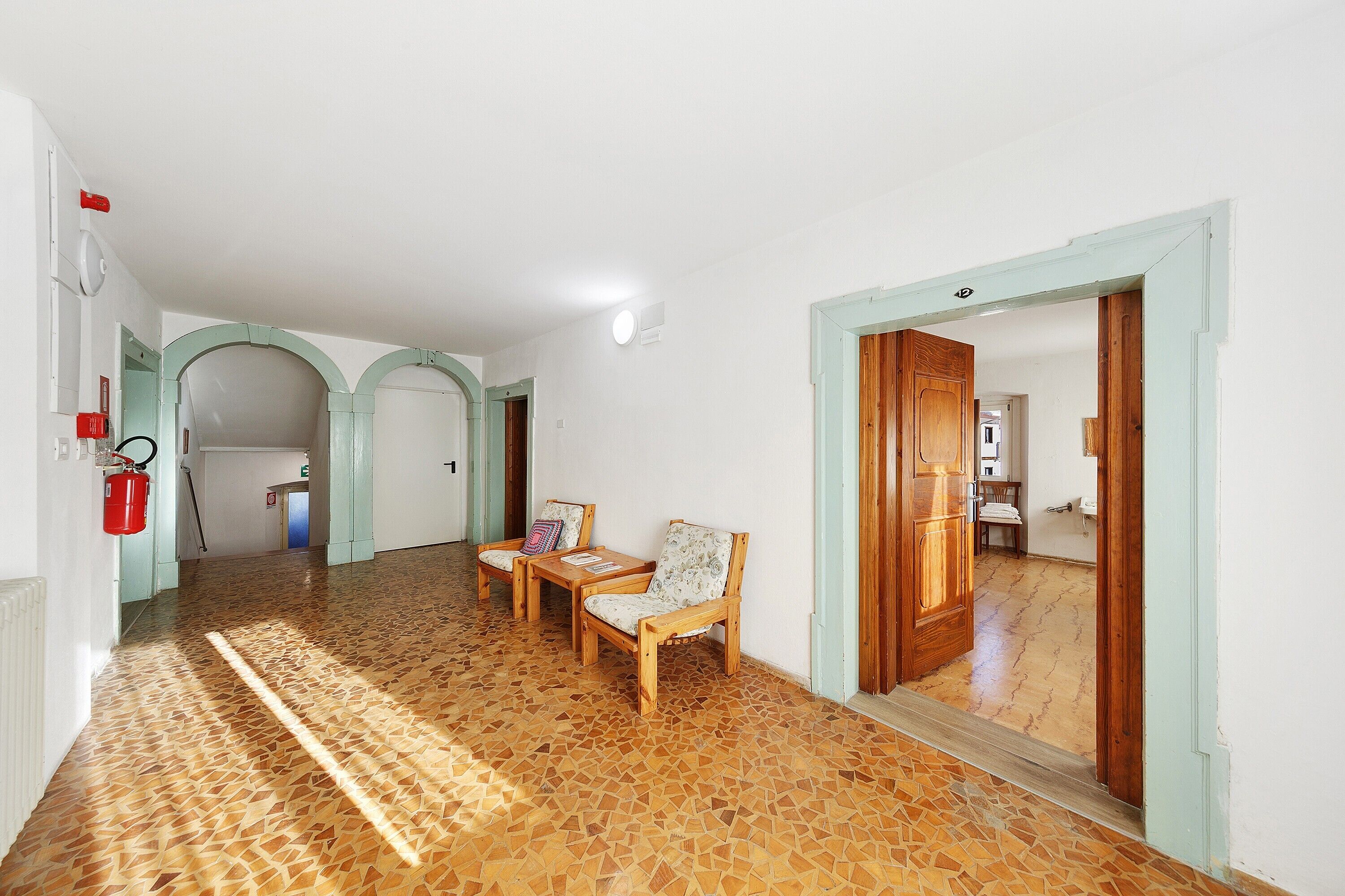 Un pasillo con piso estampado, sillas de madera y una puerta que da a otra habitación.