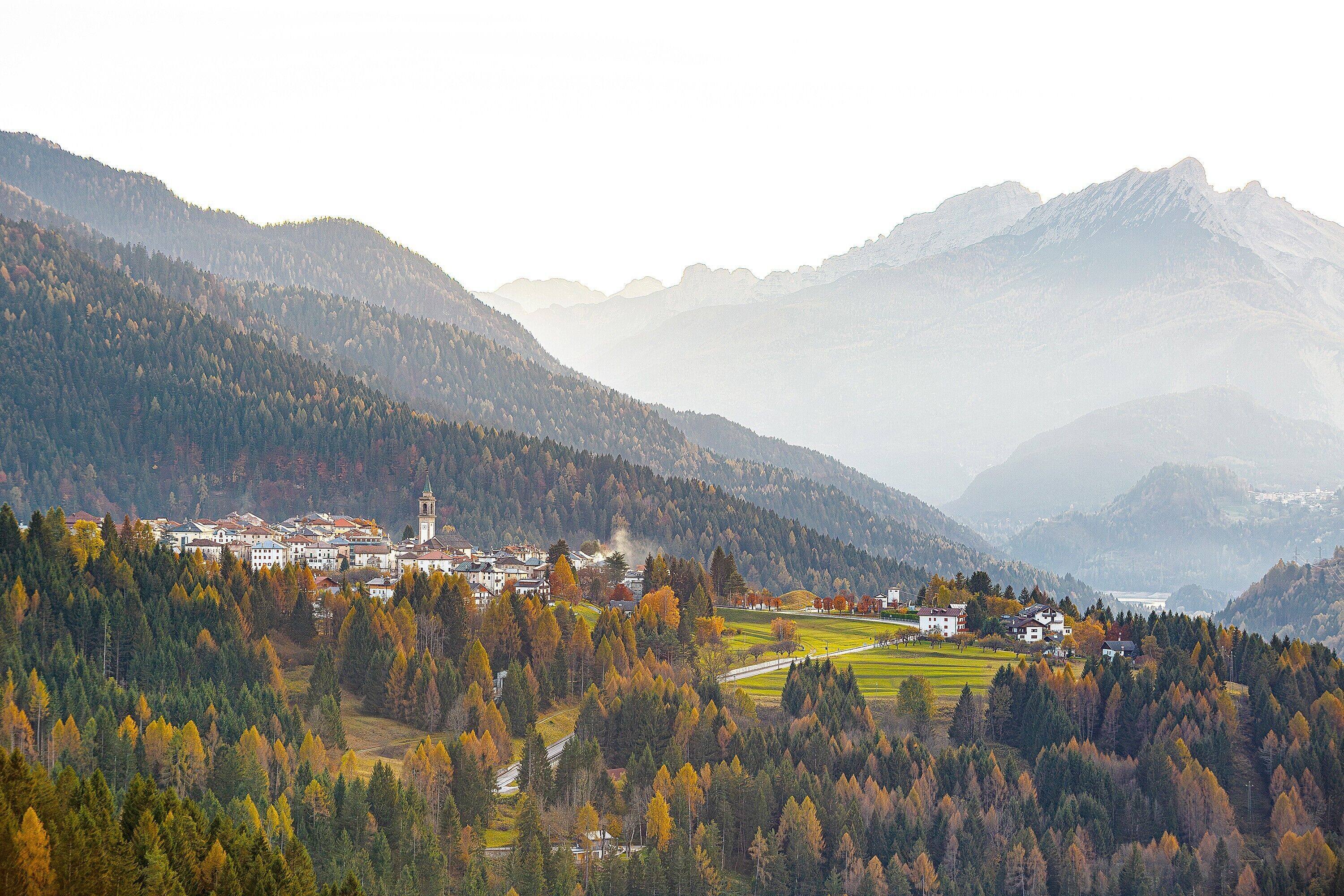 A mountainous landscape with a village, buildings, and autumn foliage.