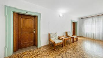 Una habitació amb una porta de fusta, dues cadires, una taula petita i un paviment amb dibuixos.