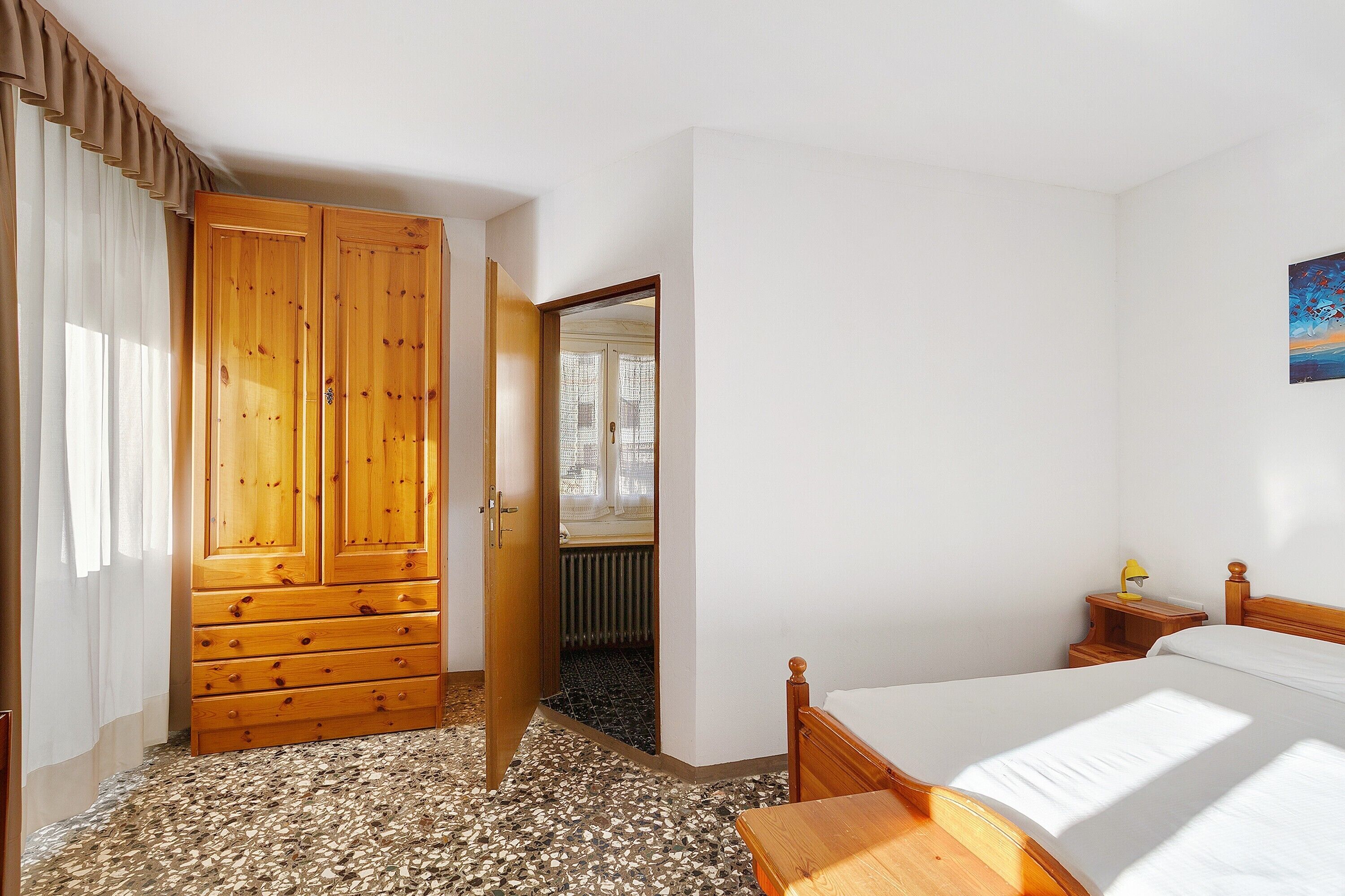 Een slaapkamer met een houten garderobe, een bed, een nachtkastje en een spiegel.