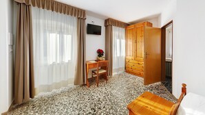 A room with a wooden desk, a chair, a television on the wall, and a wardrobe.