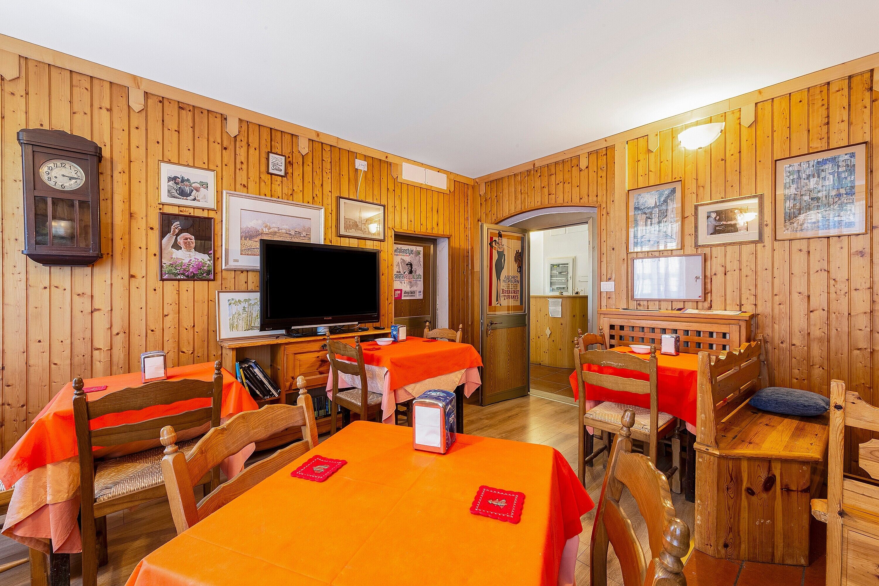 A dining area with wooden walls, tables with orange tablecloths, and a television.
