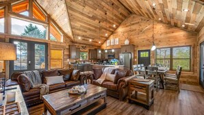 A spacious living area with a large wooden ceiling, a cozy fireplace, and a dining area with a wooden table and chairs. - Stunning Mtn Views | Hot Tub | Game Room | EV (Sevierville)