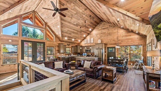 A spacious wooden cabin with a high ceiling, large windows, a cozy living area with a fireplace, and a separate kitchen area. - Stunning Mtn Views | Hot Tub | Game Room | EV (Sevierville)