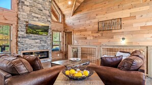 A cozy room with a stone fireplace, leather sofas, and a table with a fruit bowl. - Stunning Mtn Views | Hot Tub | Game Room | EV (Sevierville)