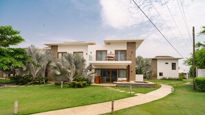 A modern two-story house with a well-maintained lawn, a patio with outdoor furniture, and a clear sky. - Luxury Villa w Direct Pool Entry Monterrico (Taxisco)