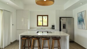 A modern kitchen with a central island, bar stools, a refrigerator, and a window with a view. - Luxury Villa w Direct Pool Entry Monterrico (Taxisco)