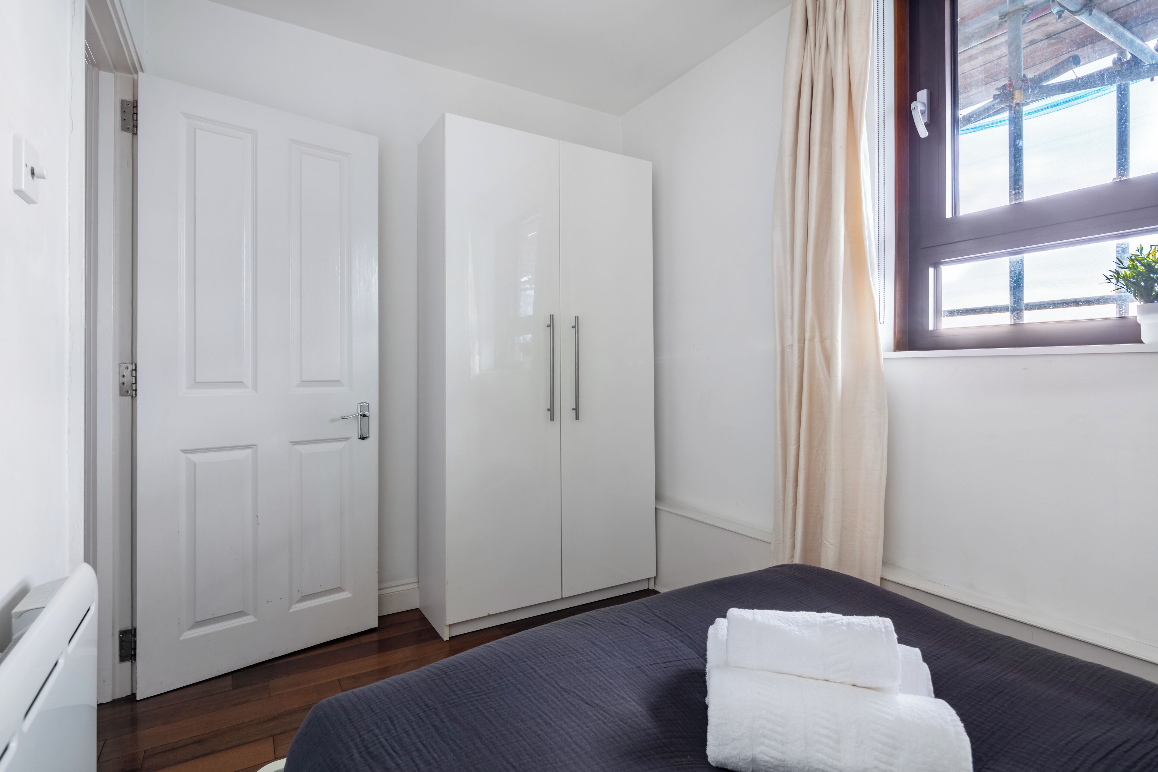 A bedroom with a bed, a wardrobe, a window with a plant, and a door.