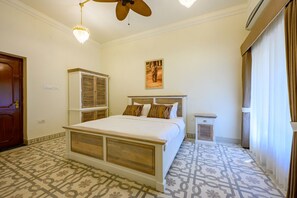 Um quarto com uma cama, um ventilador de teto, uma mesa de cabeceira, um aquecedor fixado na parede e pisos revestidos com ladrilhos estampados.