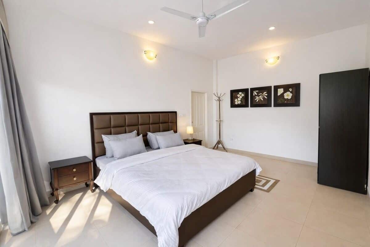 A bedroom with a bed, bedside tables, a floor lamp, and artwork on the wall.