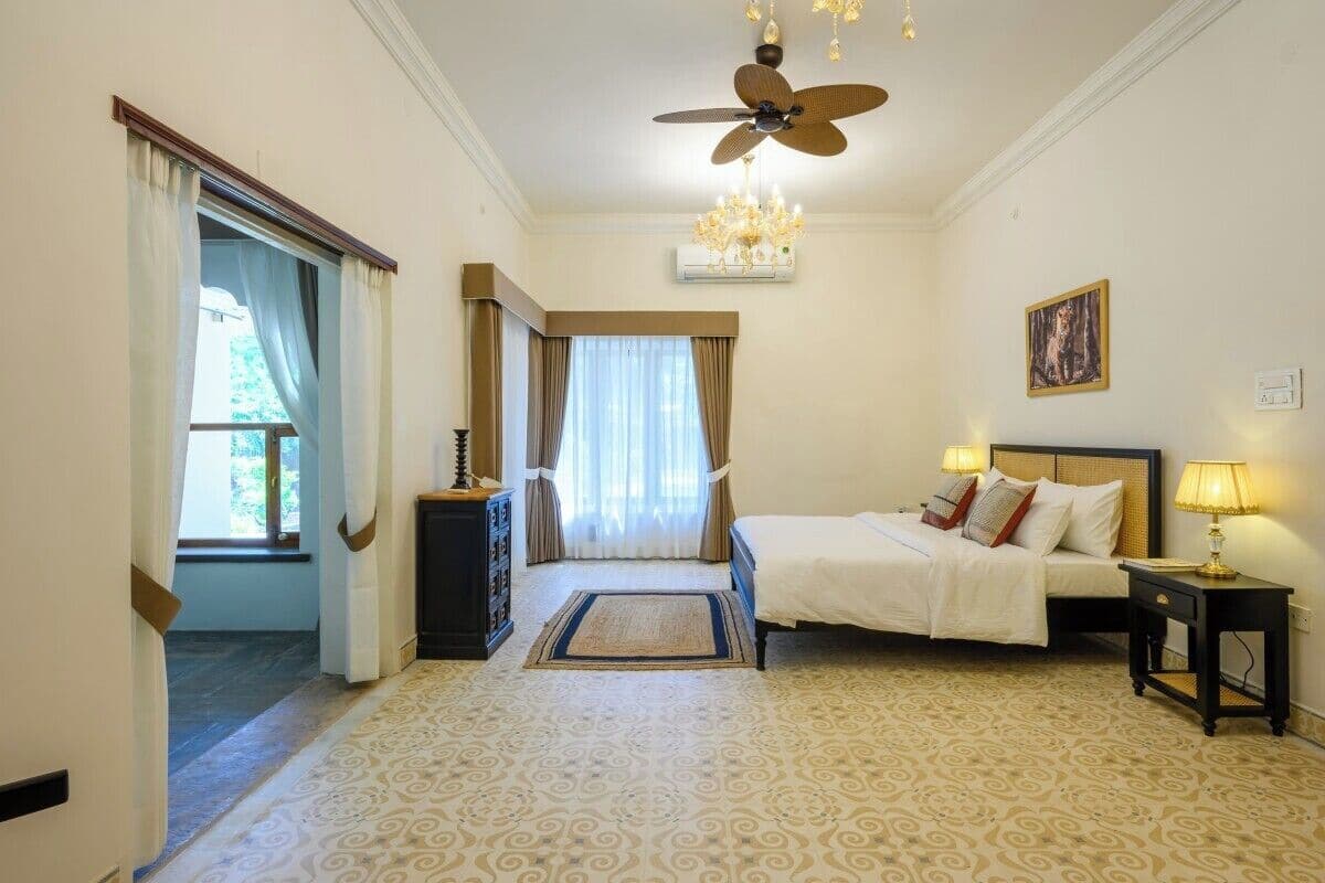 A hotel room with a bed, bedside tables, a ceiling fan, a chandelier, and a window with curtains.