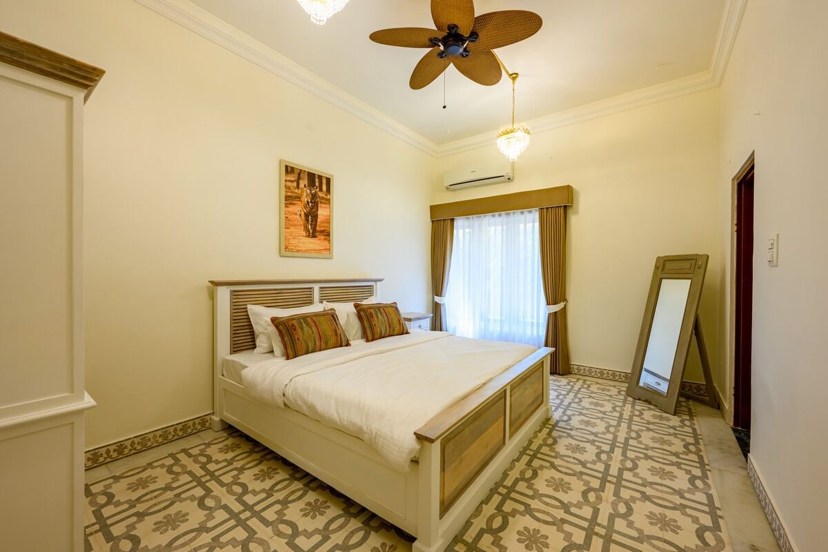 A bedroom with a bed, a ceiling fan, a window with curtains, and a mirror.