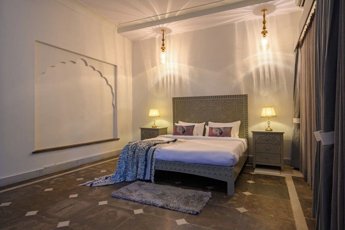 A bedroom with a bed, two bedside tables, a large wall art piece, and a patterned rug.