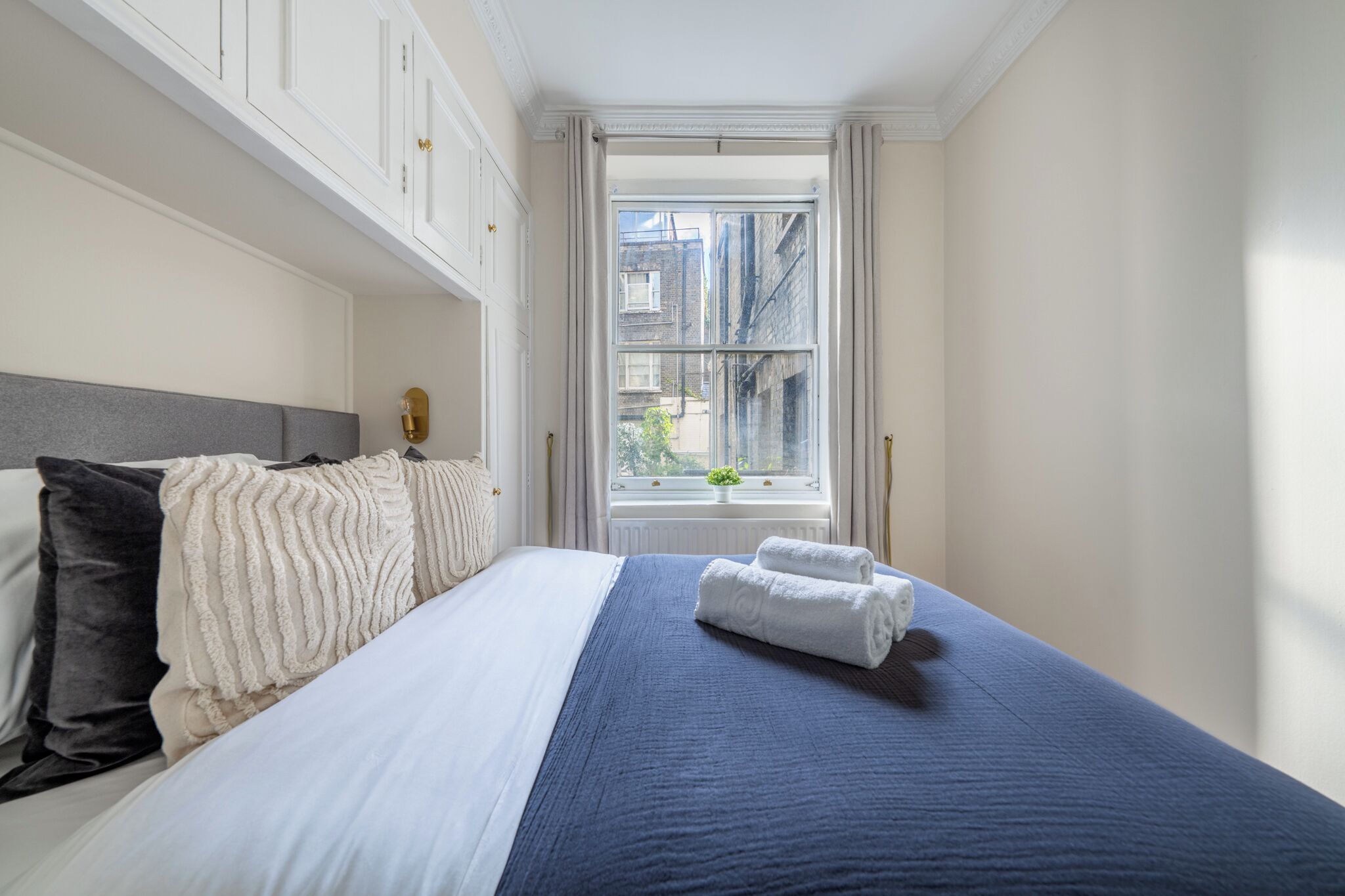 Un lit bien fait, avec une couette bleue et blanche, une tête de lit grise et deux serviettes enroulées posées sur le lit.