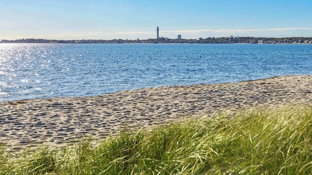 Una spiaggia con vista chiara sullo skyline di una città lontana, con una torre ben visibile.