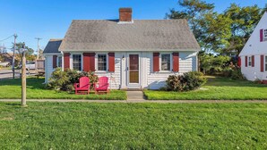 Una casa a un piano con tetto a due falde, un portico con due poltrone rosse Adirondack e un piccolo giardino anteriore.