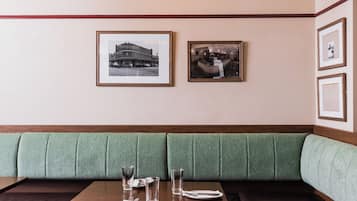 Un restaurant avec des banquettes recouvertes d’un tissu vert, des photographies encadrées accrochées au mur et une table dressée avec des assiettes, des verres et des couverts.