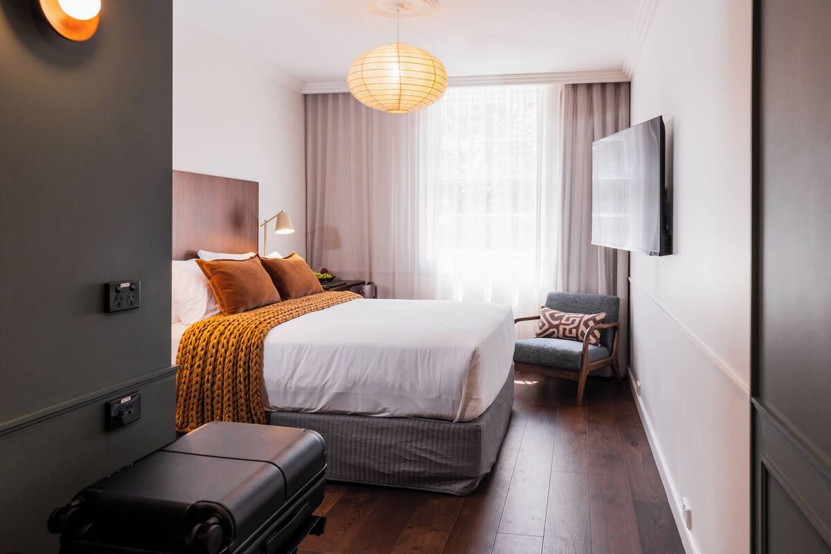 Une chambre d’hôtel avec un lit, une chaise, une télévision et une valise.