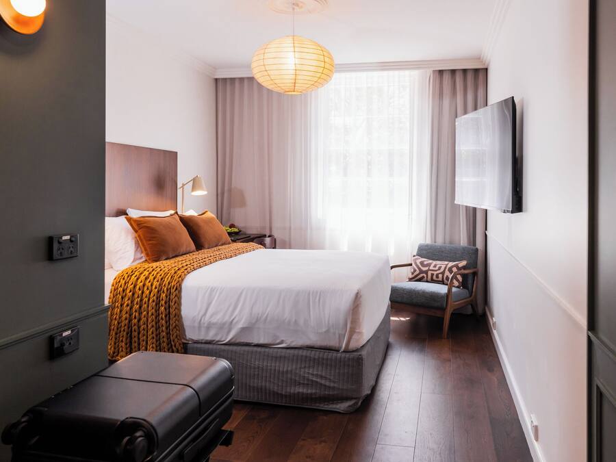 A hotel room with a bed, a chair, a TV, and a suitcase.