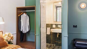 Una camera d'albergo con un letto, un armadio in legno, un bagno con lavandino e specchio, e una valigia sul pavimento.