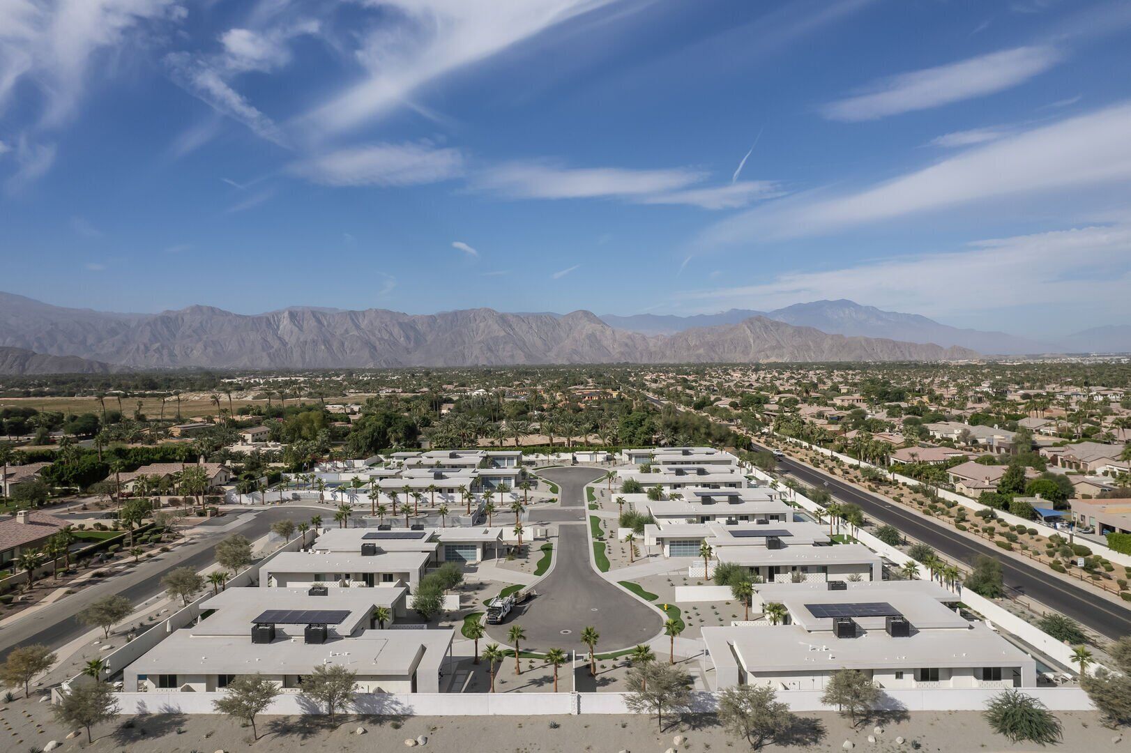 Zona residencial moderna com uma rua central, rodeada por casas e vegetação, com montanhas ao fundo.