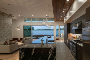 A modern kitchen with a marble island, built-in appliances, and a view of a lake. - Gold @ Elemento49 | Pool & Pickleball | Sleeps 18 (Indio)