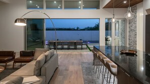 A modern kitchen with a large island, a dining area with a table and chairs, and a seating area with a sofa and chairs. - Carbon @ Elemento49 - Pool & Spa - Sleeps 16 (Indio)
