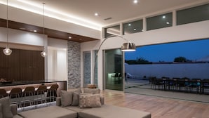 A modern living room with a sectional sofa, a dining area with bar stools, and a large sliding glass door leading to an outdoor patio. - Neon @ Elemento49 - Pool & Spa - Sleeps 16 (Indio)