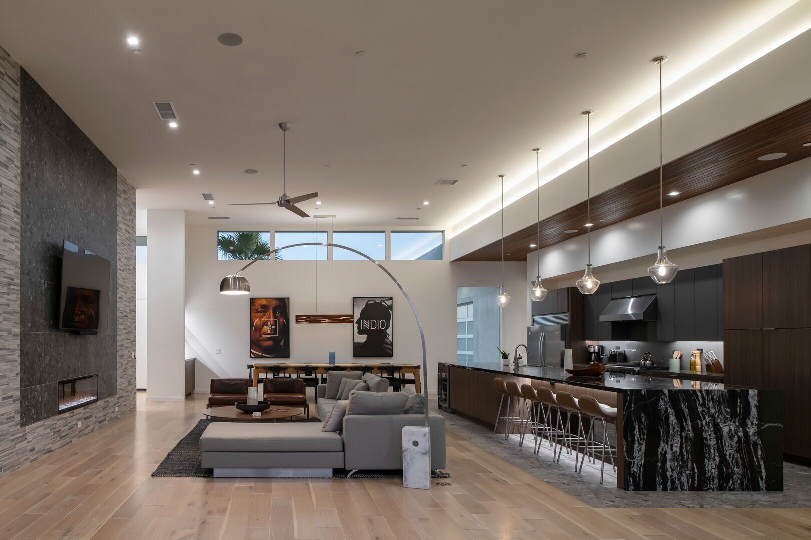 Une cuisine moderne dot ée d’un grand îlot central, de meubles de rangement aux couleurs sombres et d’un éclairage suspendu.