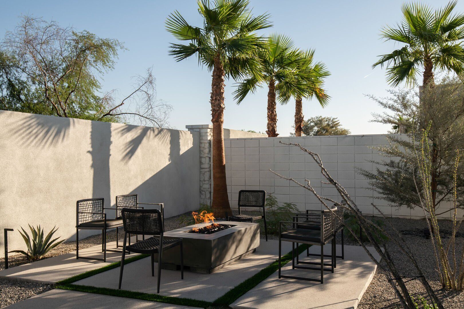 A patio area with a fire pit, seating, and palm trees.