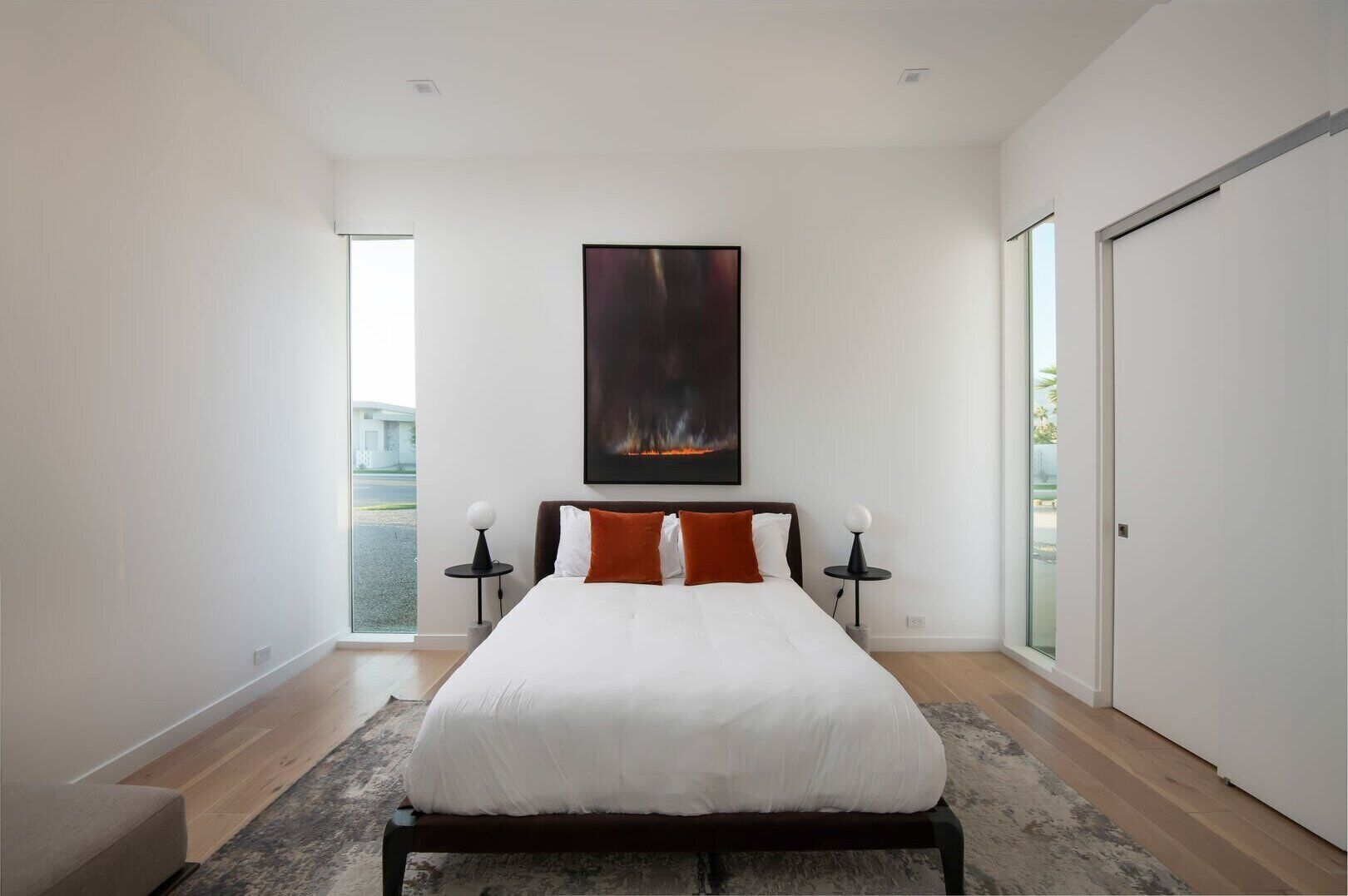 Une chambre moderne avec un grand lit, deux tables de chevet, une grande fenêtre et une porte.