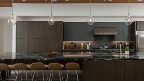 Una cucina moderna con mobili in legno scuro, un'isola in marmo e luci a sospensione.