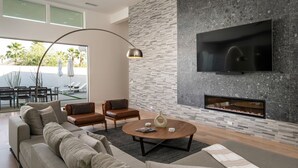 Una sala de estar moderna con chimenea, televisor montado en la pared y una zona de estar con sofá y sillones.