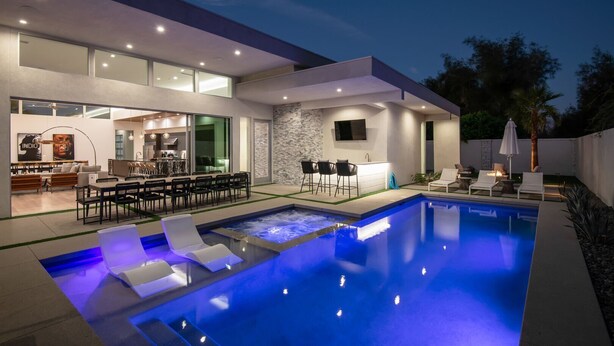 Un área de piscina moderna al aire libre con bar y asientos, rodeada por un patio bien iluminado y un muro de piedra.