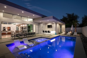A modern outdoor pool area with a bar and seating, surrounded by a well-lit patio and a stone wall. - Silver @ Elemento49 - Pool & Spa - Sleeps 16 (Indio)