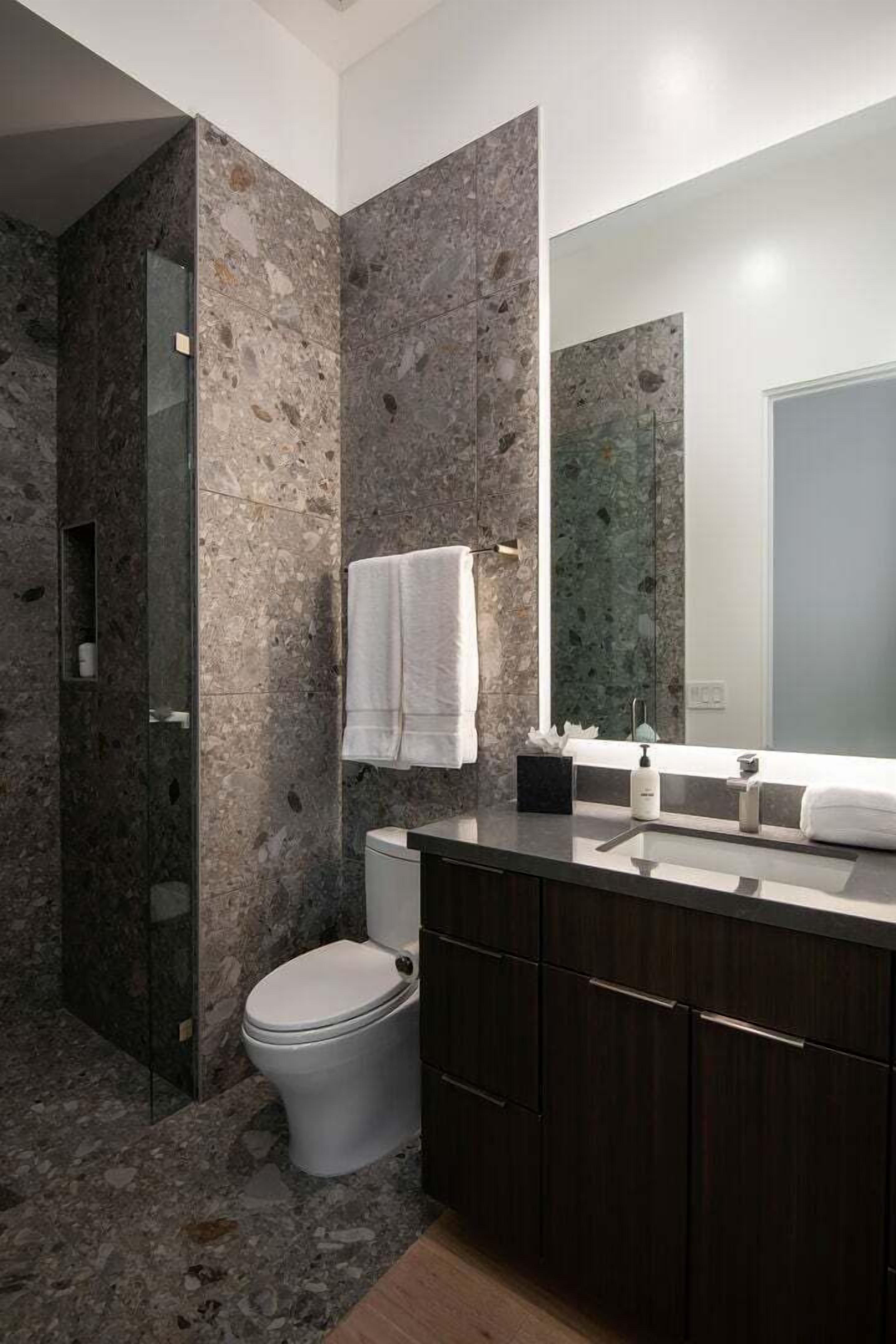 A modern bathroom with a marble wall, a toilet, a sink with a mirror, and a shower area.