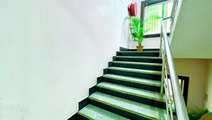 A staircase with a handrail, a potted plant, and a window with green blinds. - Hotel President Inn -near Temple & Beach (Puri)